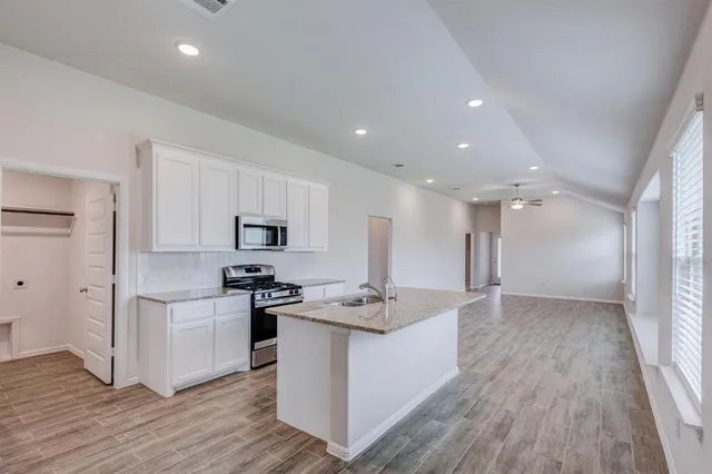 a kitchen with stainless steel appliances granite countertop a stove top oven a sink a refrigerator and white cabinets with wooden floor