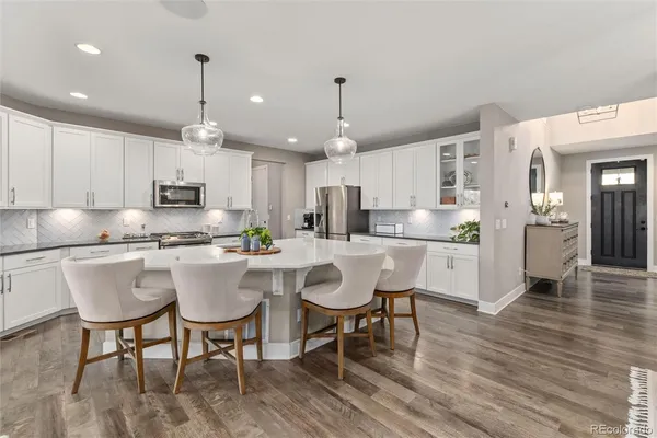 a kitchen with stainless steel appliances granite countertop a dining table chairs refrigerator and microwave