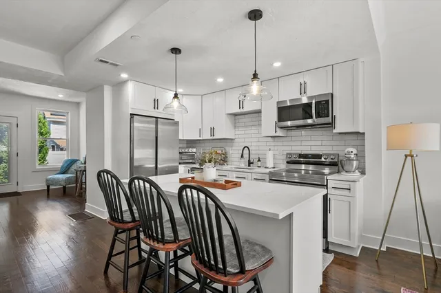 a kitchen with stainless steel appliances a stove a sink a refrigerator a kitchen island a stove a kitchen island a table and chairs with wooden floor