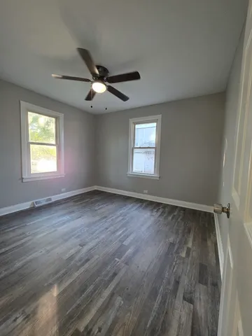 an empty room with wooden floor ceiling fan and windows