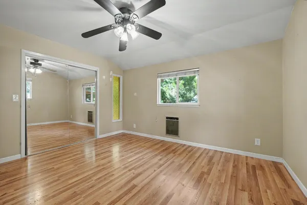 a view of an empty room with wooden floor and a ceiling fan