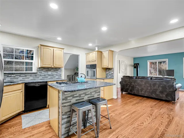 a kitchen with stainless steel appliances granite countertop a stove a sink dishwasher a refrigerator and white cabinets with wooden floor