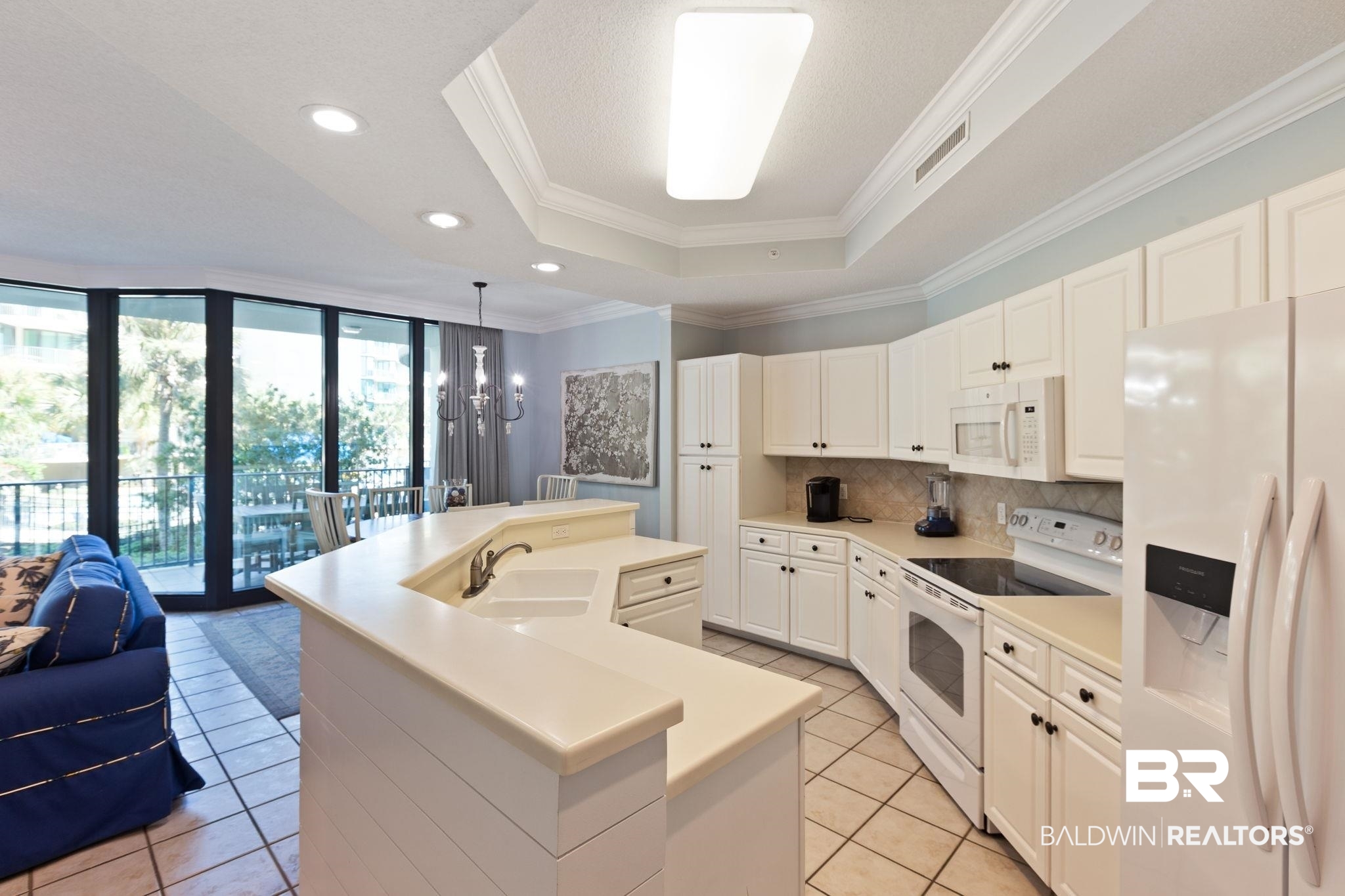 27580 Canal Road, Unit 1112 Orange Beach, AL 36561 - Photo 8 of 50 Kitchen with white appliances, a tray ceiling, an island with sink, a chandelier, and crown molding