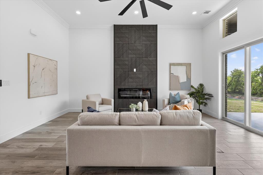 182 Briar Patch Azle, TX 76020 - Photo 7 of 36 Living room with a large fireplace, light wood-style floors, crown molding, a high ceiling, and a ceiling fan
