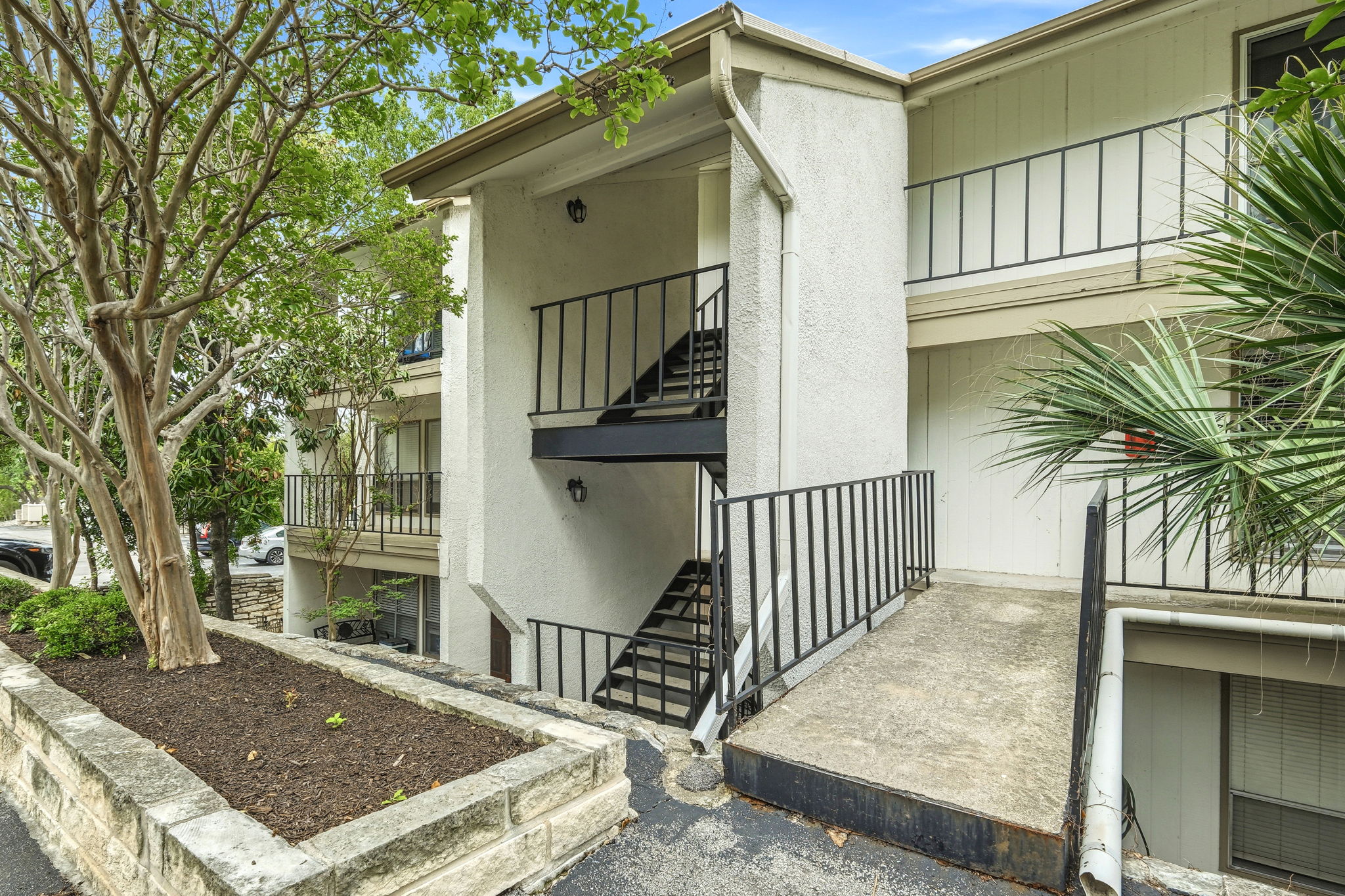 6910 Hart Lane, Unit 912 Austin, TX 78731 - Photo 20 of 36 Multi-level building exterior featuring white stucco and siding, black metal railings, and a concrete pathway with stone planter boxes