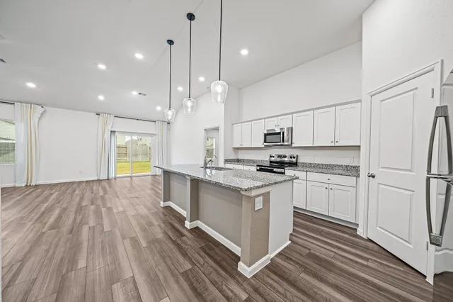 a kitchen with stainless steel appliances granite countertop a refrigerator a stove a sink and white cabinets with wooden floor