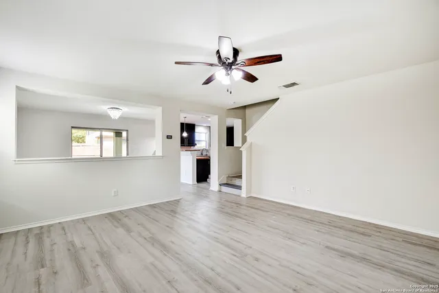 an empty room with wooden floor a ceiling fan and windows