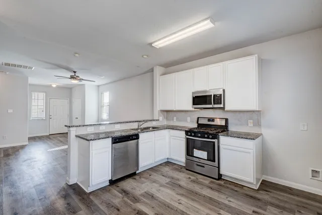 a kitchen with stainless steel appliances granite countertop a stove top oven a sink and white cabinets