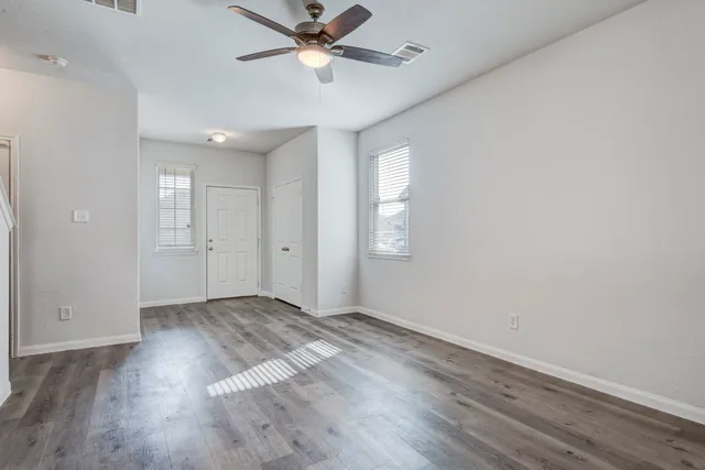 an empty room with wooden floor fan and windows