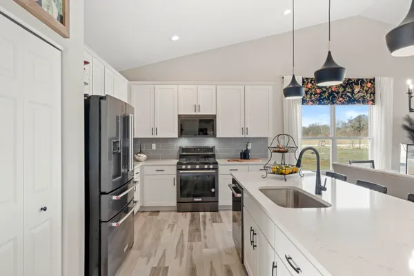 a kitchen with stainless steel appliances granite countertop a refrigerator a sink dishwasher a stove and a dining table with wooden floor