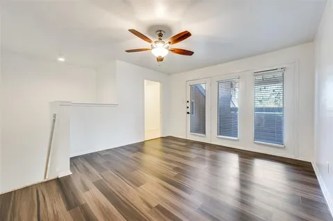 a view of an empty room with wooden floor and a ceiling fan
