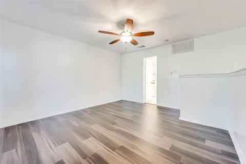 an empty room with wooden floor fan and windows