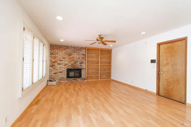 a view of an empty room with wooden floor fireplace and a window