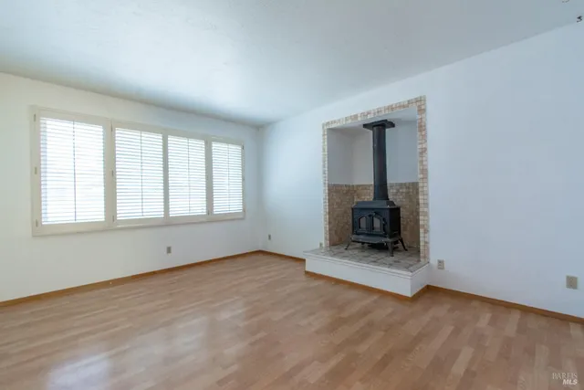 an empty room with wooden floor fire place and windows