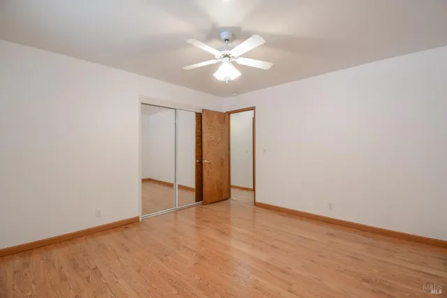 a view of an empty room with wooden floor and a ceiling fan