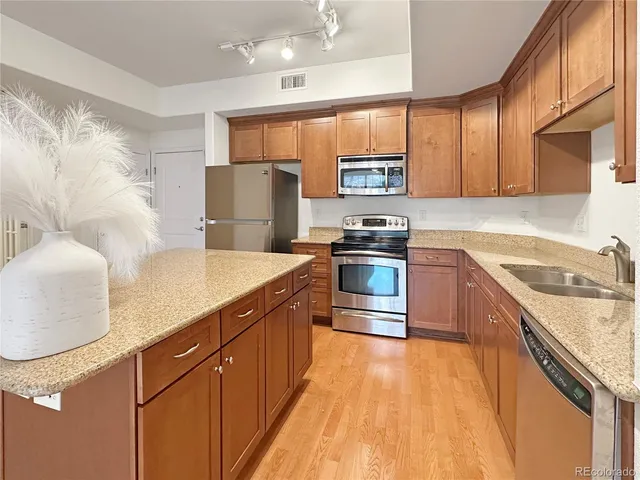 a kitchen with stainless steel appliances granite countertop a refrigerator a stove and a sink with wooden floor