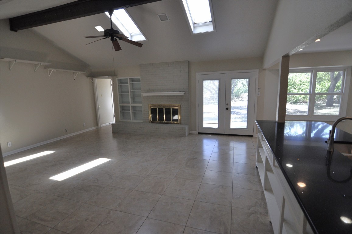 13203 Stillforest Street Austin, TX 78729 - Photo 4 of 24 Unfurnished living room with a brick fireplace, ceiling fan, a skylight, beam ceiling, and french doors