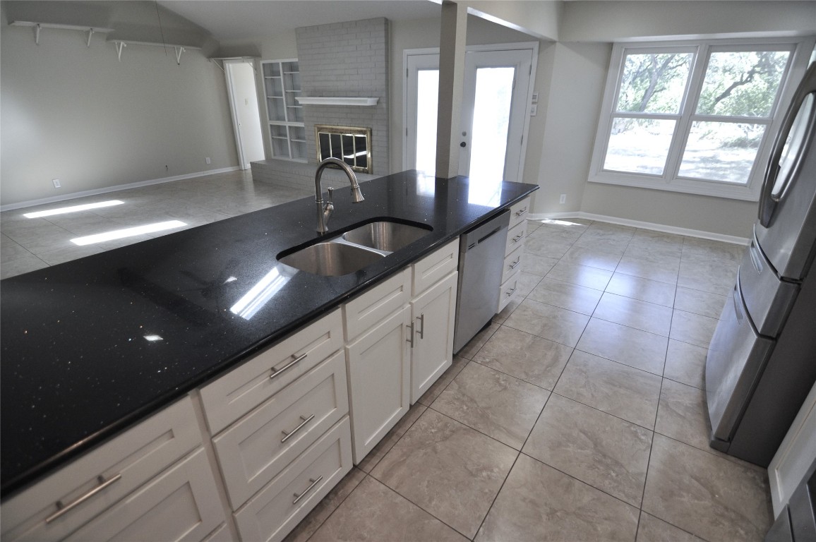 13203 Stillforest Street Austin, TX 78729 - Photo 8 of 24 Kitchen with white cabinetry, light tile patterned floors, stainless steel appliances, a fireplace, and dark stone counters