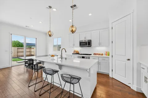 a very nice looking kitchen with granite countertop a stove a sink a dining table and chairs with wooden floor