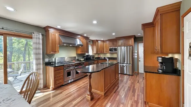 a kitchen with stainless steel appliances granite countertop a refrigerator a stove top oven a sink dishwasher and wooden cabinets with wooden floor