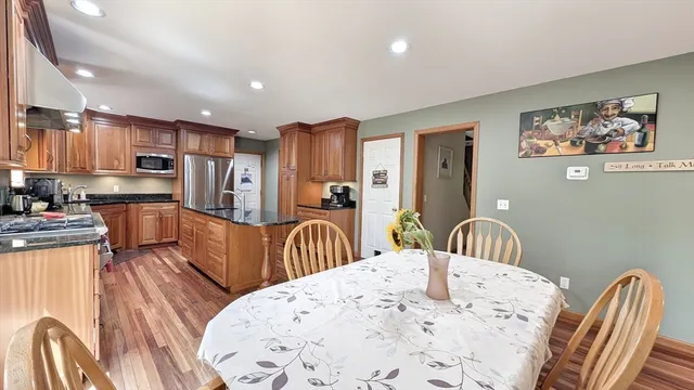 a kitchen with stainless steel appliances kitchen island granite countertop a refrigerator a sink a stove a dining table and chairs with wooden floor