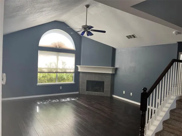 an empty room with wooden floor fireplace and windows