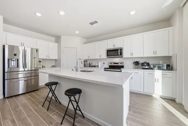 a kitchen with granite countertop a refrigerator stove a sink and white cabinets with wooden floor