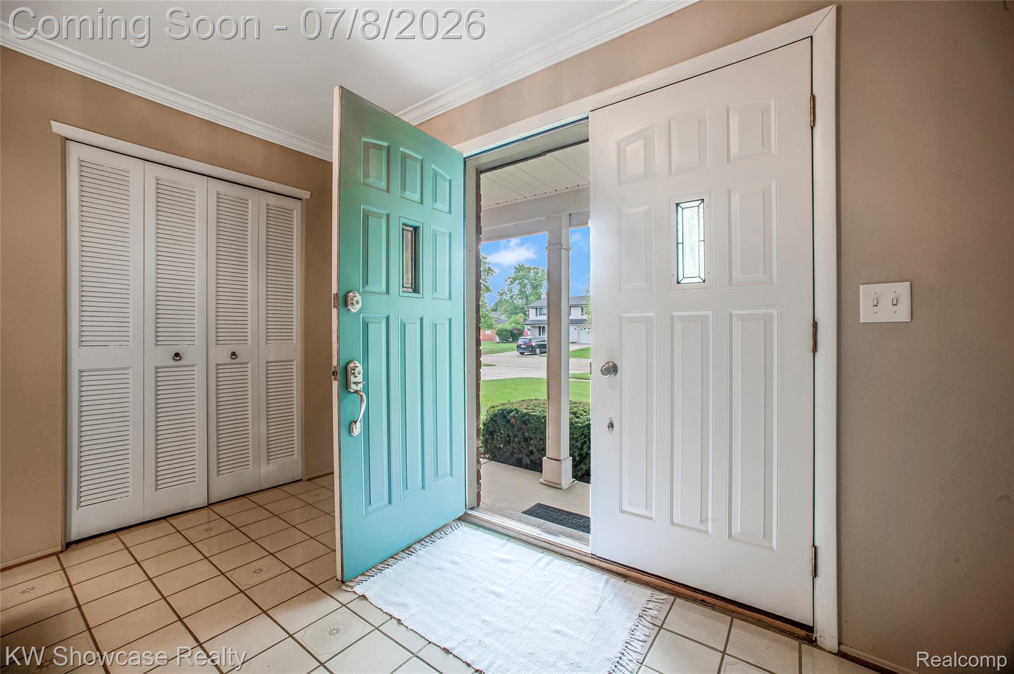 16720 Wayne Road Livonia, MI 48154 - Photo 6 of 29 Inviting entryway featuring a teal front door with a decorative glass insert, a white storm door, louvered bi-fold closet doors, cream-colored tile flooring, and crown molding