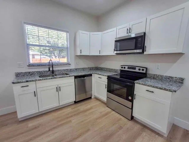 a kitchen with stainless steel appliances granite countertop white cabinets a sink a stove a microwave and wooden floors