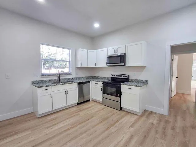 a kitchen with granite countertop a stove top oven a sink dishwasher and a microwave with wooden floor