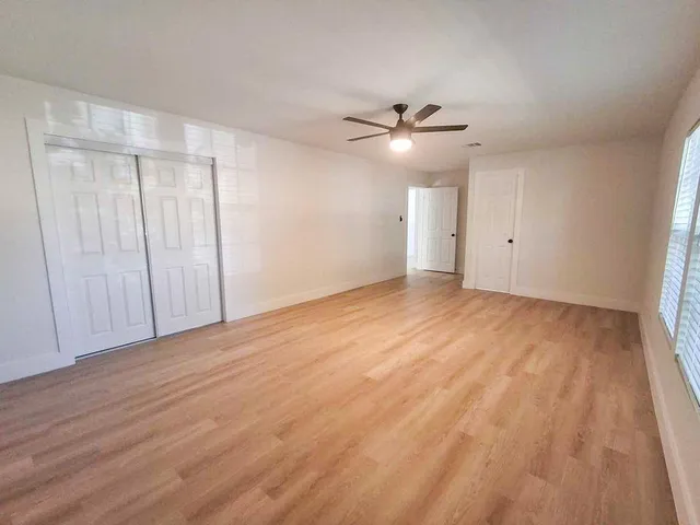 an empty room with wooden floor fan and windows