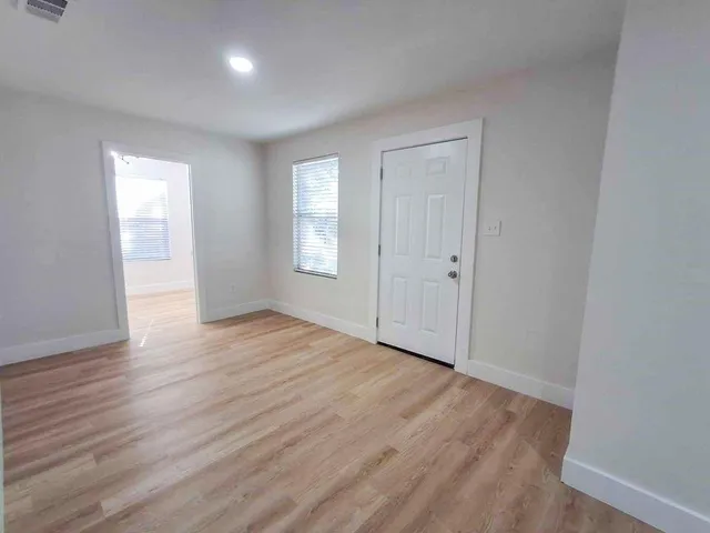 a view of an empty room with wooden floor and window
