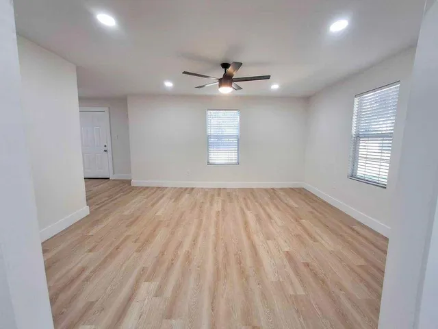 an empty room with wooden floor ceiling fan and windows