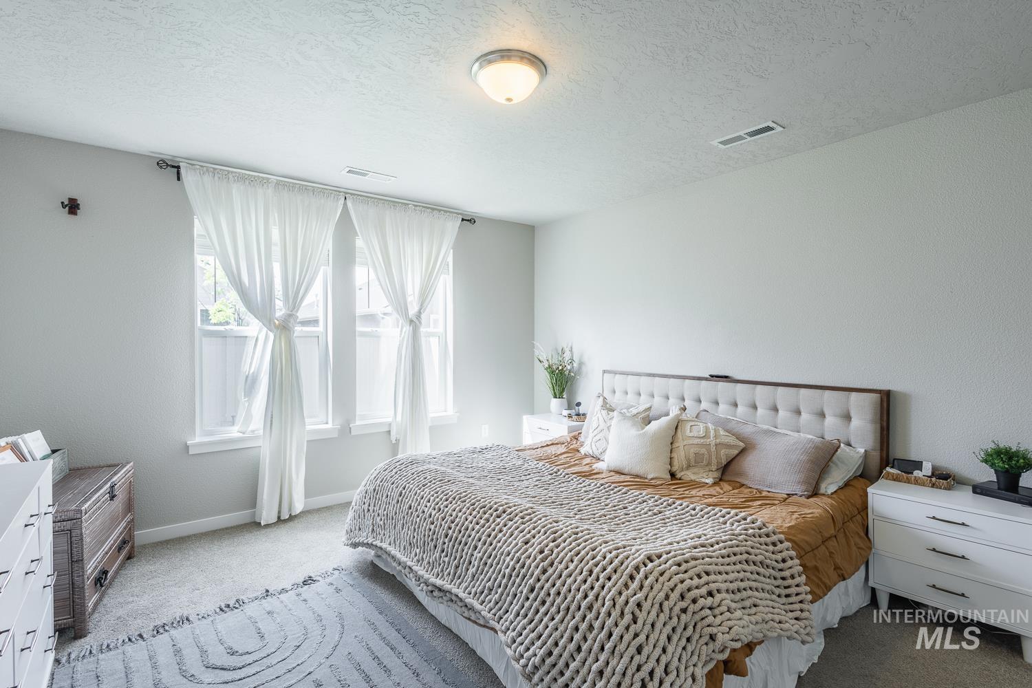 12623 Shadow Peak Street Caldwell, ID 83607 - Photo 25 of 50 Carpeted room featuring a tufted upholstered headboard, multiple windows with white sheer curtains, and a flush mount ceiling light fixture