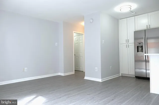 a view of an empty room with wooden floor and a kitchen