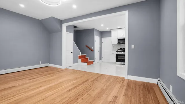 an empty room with wooden floor and way to kitchen