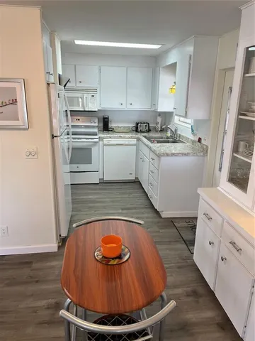 a kitchen with stainless steel appliances kitchen island granite countertop a sink a stove a refrigerator and white cabinets with wooden floor