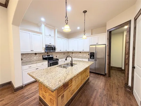 a kitchen with stainless steel appliances granite countertop a refrigerator a sink dishwasher a stove and white countertops with wooden floor