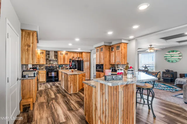 a kitchen with stainless steel appliances kitchen island granite countertop a refrigerator a stove a sink dishwasher a couches with wooden cabinets and wooden floor