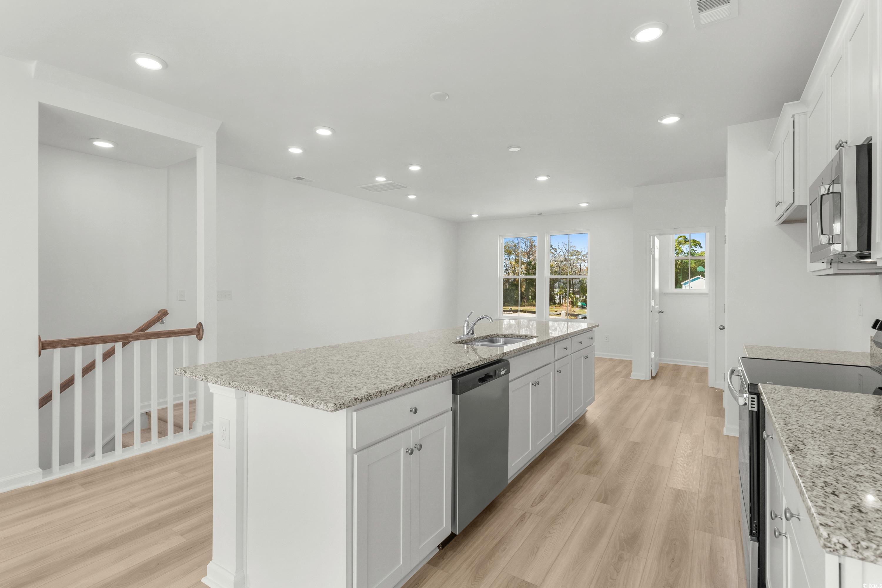 4414 Kingsport Road, Unit 1502 Little River, SC 29566 - Photo 9 of 33 Kitchen featuring white cabinetry, light stone counters, stainless steel appliances, a center island with sink, and light wood finished floors