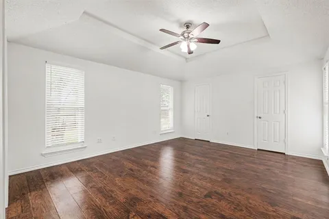 an empty room with wooden floor chandelier fan and windows