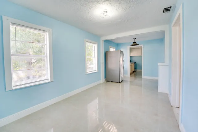 an empty room with windows and refrigerator
