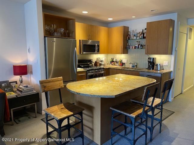 a kitchen with stainless steel appliances granite countertop a dining table chairs refrigerator and sink
