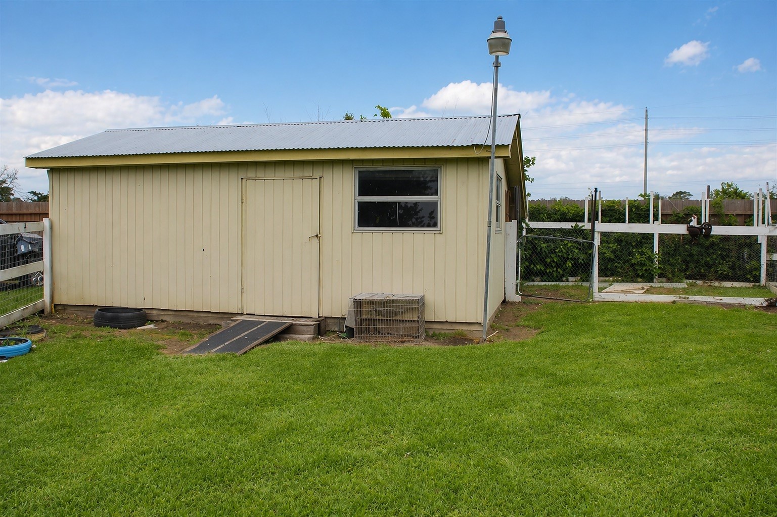 206 Riverside Street Highlands, TX 77562 - Photo 11 of 12 Versatile standalone workshop with cream siding, metal roof, windows, and exterior pole lighting, perfect for hobbies, storage, or a dedicated workspace all tucked within the spacious backyard.