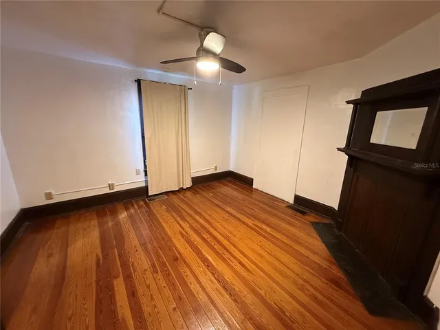 a view of an empty room with wooden floor and a ceiling fan