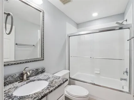 a bathroom with a granite countertop bathtub shower sink vanity and toilet