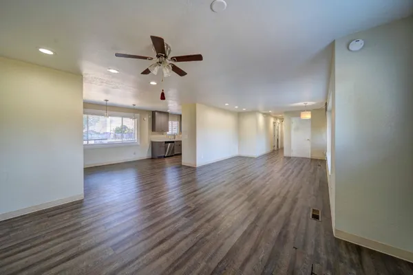 a view of an empty room and a kitchen with wooden floor and a ceiling fan