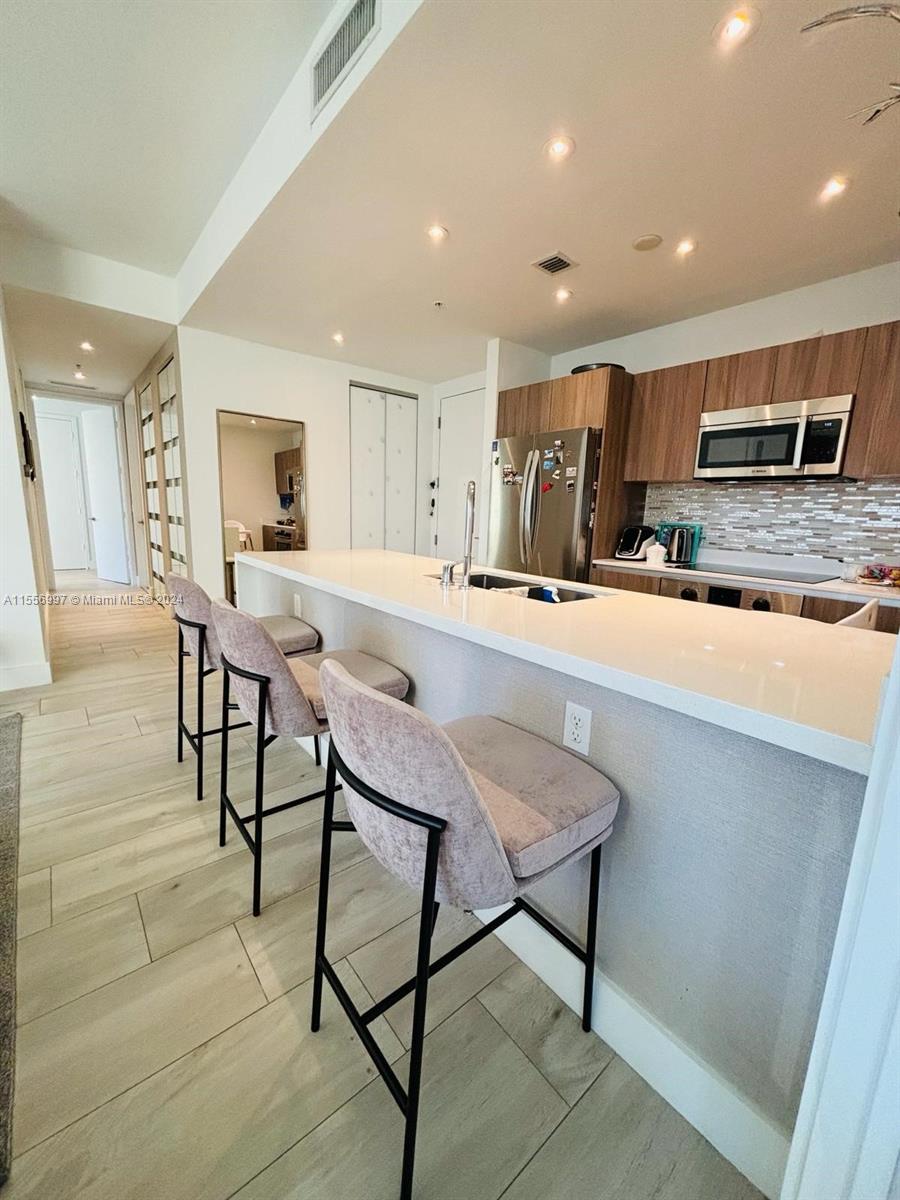 a kitchen with stainless steel appliances kitchen island granite countertop a stove a sink a oven a dining table and chairs with wooden floor