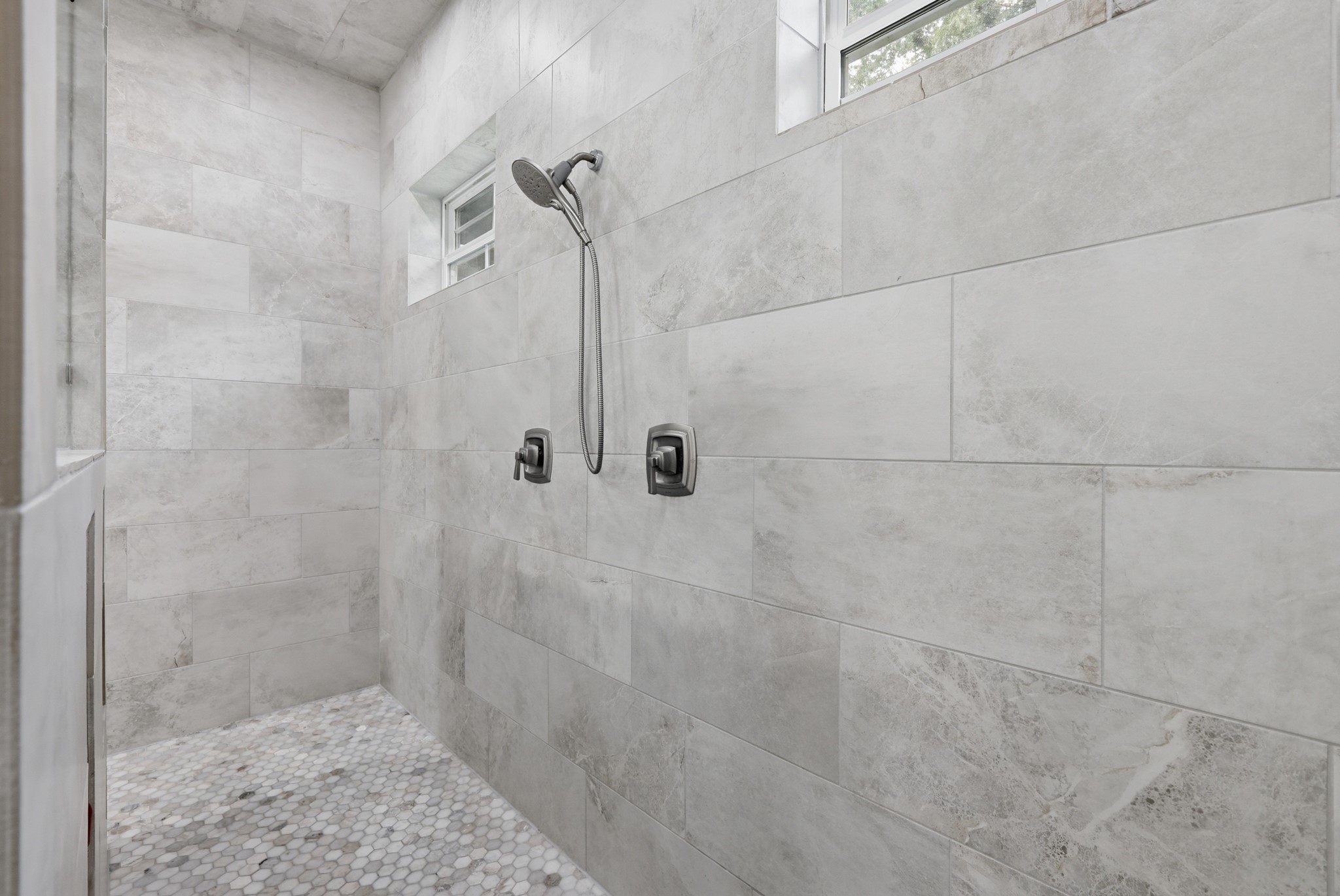 7106 Hampton Court Spring, TX 77389 - Photo 13 of 31 Modern, spacious shower with sleek, neutral-toned tiles and a rainfall showerhead. Natural light filters in through small, high windows, enhancing the clean and contemporary design.