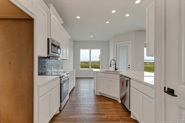 a large kitchen with stainless steel appliances a sink and white cabinets